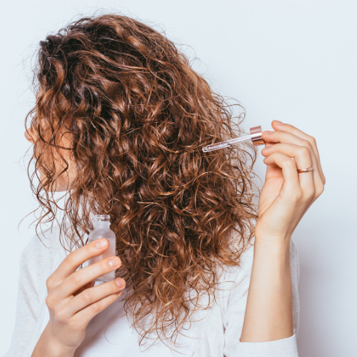 Woman applying serum to curly hair for hair thinning routine, gentle organic scalp care, Canadian clean beauty DR.MESO